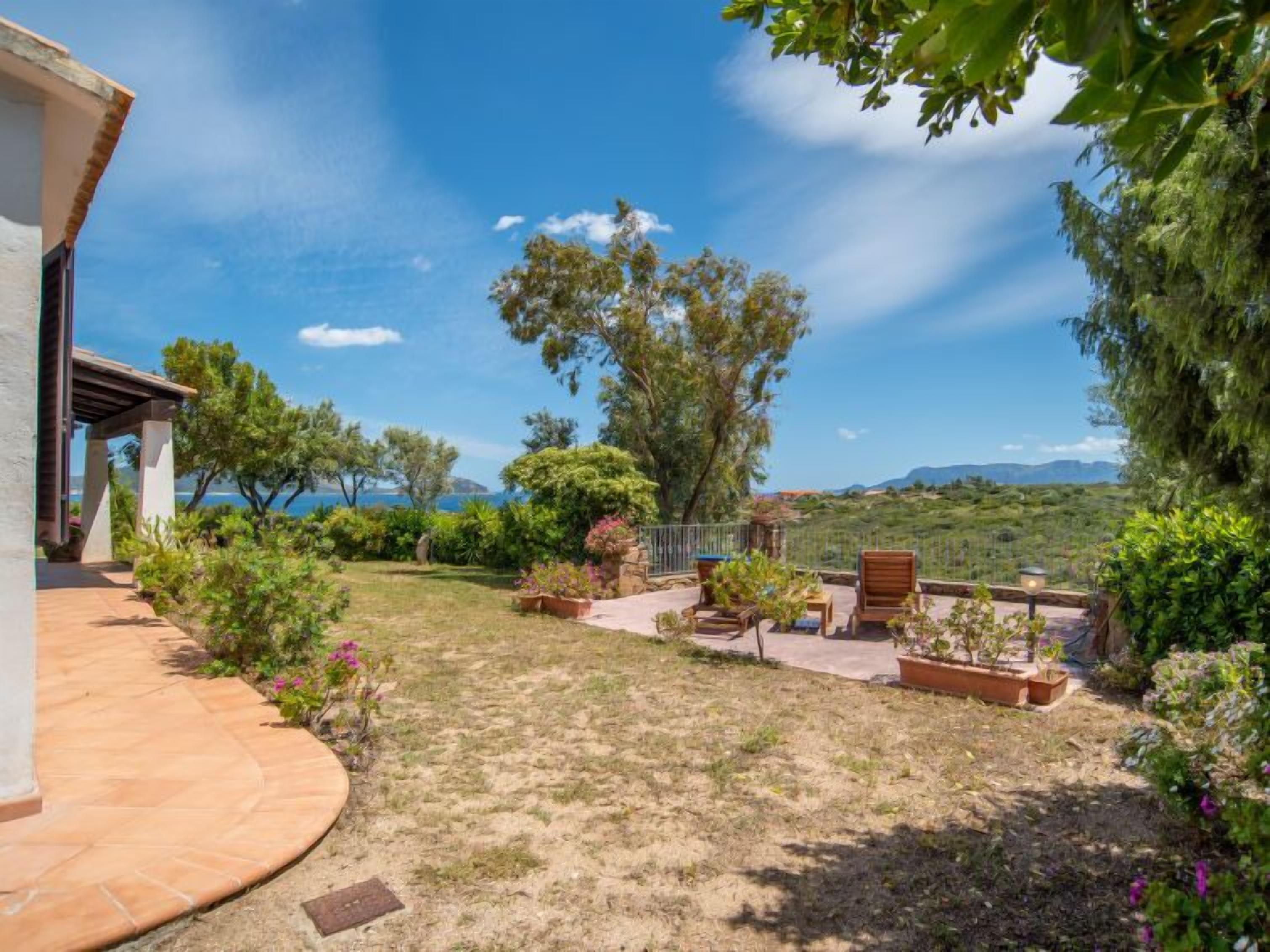 Eine Terrasse mit Sitzgelegenheiten, Blick auf das Meer und eine gebirgige Landschaft im Hintergrund.
