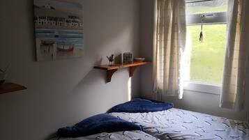 A bedroom with a bed, a window with curtains, a painting on the wall, and a shelf with items.
