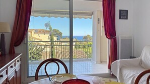 Een eethoek met een tafel voor twee personen, uitzicht op zee door een glazen deur en een balkon met een balustrade.