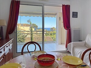 A dining area with a table set for two, a view of the sea through a glass door, and a balcony with a railing. - Les Calanques du Parc by Interhome (Saint Aygulf)