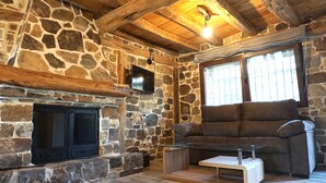 Lareira de pedra, um sofá e uma televisão num quarto rústico.
