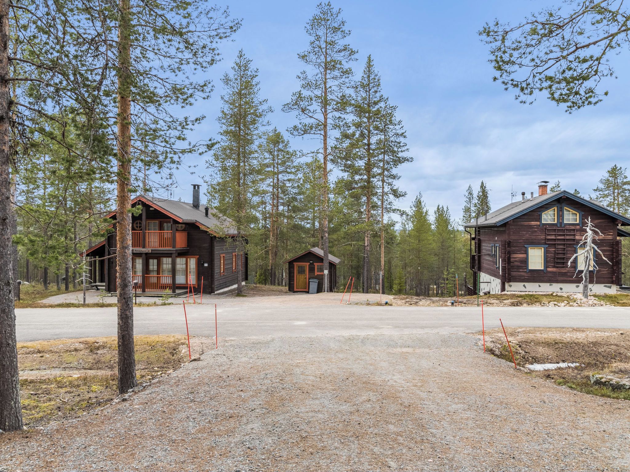 A cabin complex with multiple buildings, a gravel driveway, and surrounding trees.