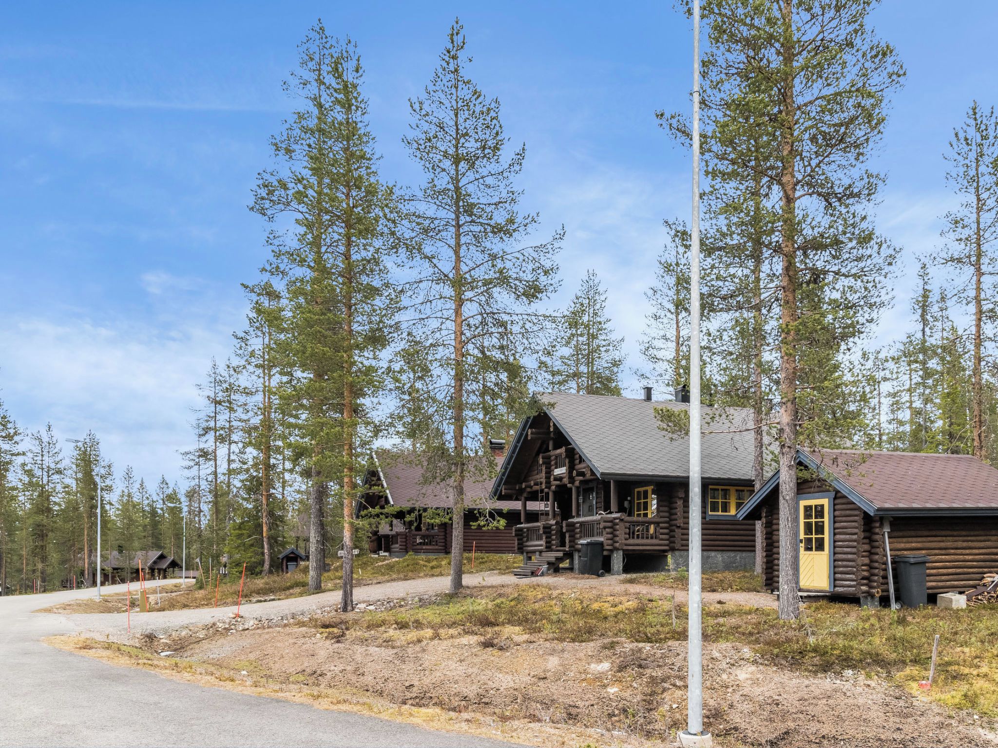Une cabane rustique en rondins de bois, dotée d’un porche et entourée de grands pins.