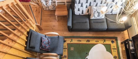 Ein gemütliches Blockhaus-Interieur mit Holzbalkendecke, einer Couch mit Kissen zum Thema Wald, einem gemusterten Teppich und einem kleinen Tisch.