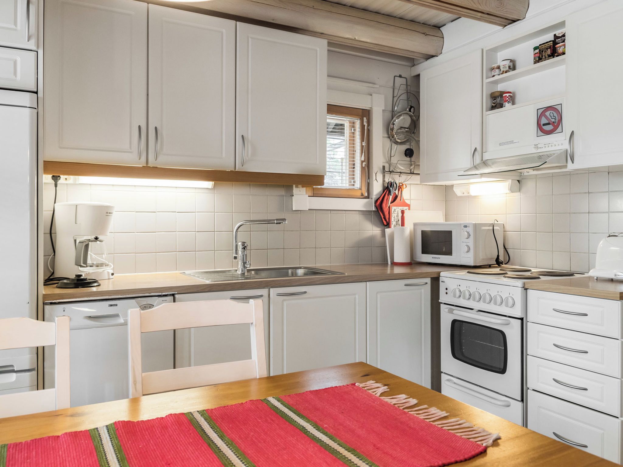 A compact kitchen with white cabinets, a built-in oven, a microwave, and a coffee machine.