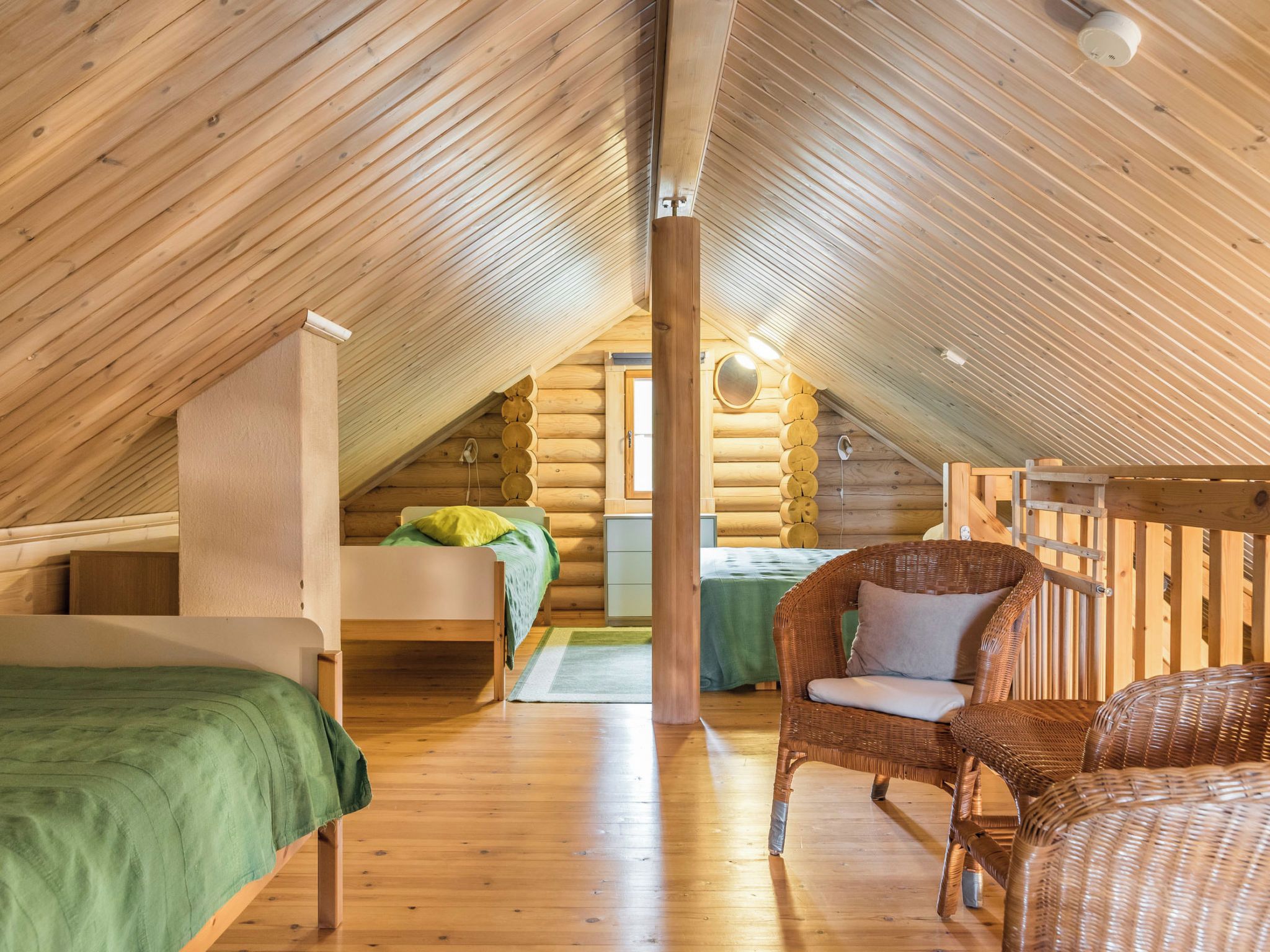 A log cabin with a loft bedroom, a green bed, a wicker chair, and a wooden floor.