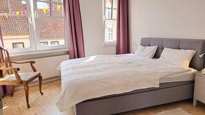 Une chambre à coucher avec un lit, une chaise, une table de chevet et une fenêtre avec des rideaux.