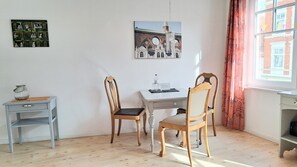 Une pièce comprenant une table à manger, deux chaises en bois, une petite table d’appoint, un tableau encadré au mur et une fenêtre avec des rideaux.