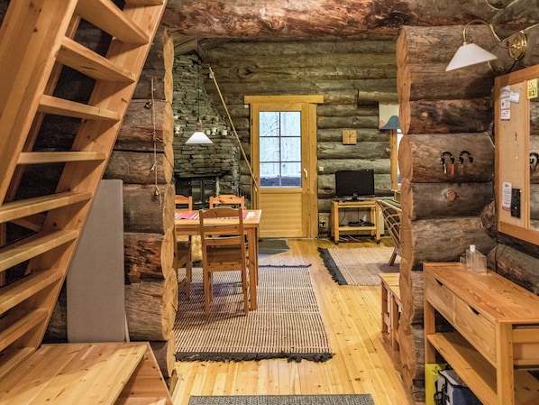 A log cabin interior with a wooden staircase, a fireplace, a television, and a door leading outside.