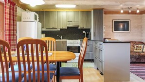 A compact kitchen with wooden cabinets, a central island, and a dining area with wooden chairs and a table. - Vacation home Ruska by Interhome (Raattama)