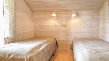 Una cabaña pequeña de una sola habitación con dos camas, paredes de madera y una ventana con cortina.