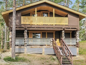 Une cabane en rondins à deux étages, dotée d’un balcon et d’un escalier menant à l’entrée.
