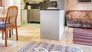A compact living space with a kitchenette, a dining area with wooden chairs, a sofa, and patterned rugs. - Vacation home Ruska by Interhome (Raattama)