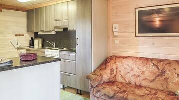 Cocina compacta con electrodomésticos modernos, horno empotrado y comedor con sofá.