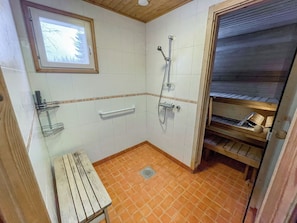 Ein kleines Badezimmer mit Fliesen, einer Dusche, einer Sitzbank und einem Ablagefach mit Pflegeprodukten.