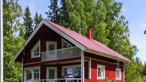 A two-story red house with a balcony, a covered porch, and two lounge chairs on the front lawn.