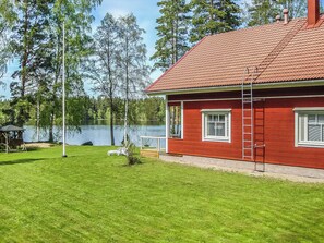 Una casa vermella amb teulada de rajola, un pati enjardinat i un llac al fons.