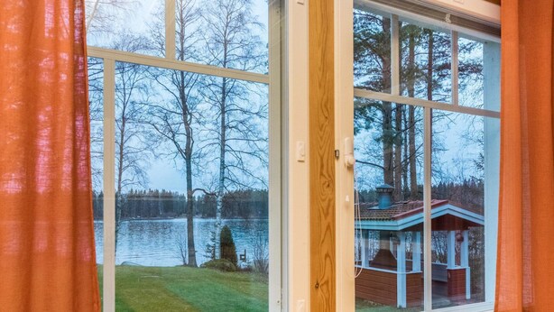 A room with a large window overlooking a lake and a wooden deck.