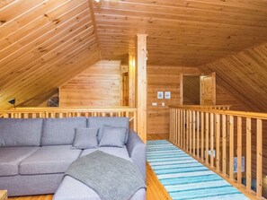 Interior d'una cabana de fusta amb un sofà, una barana de fusta i vista exterior.