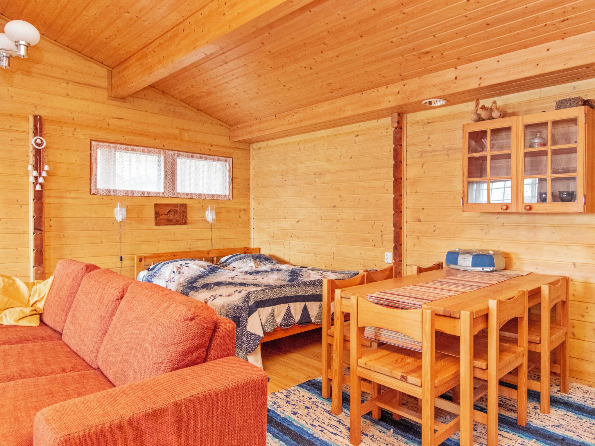 A wooden cabin interior with a bed, a sofa, a dining table, and a cabinet.