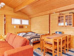 A wooden cabin interior with a bed, a sofa, a dining table, and a cabinet.