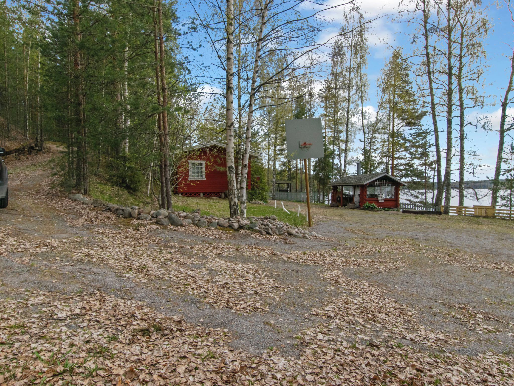 A cabin with a basketball hoop, surrounded by trees and a gravel path.