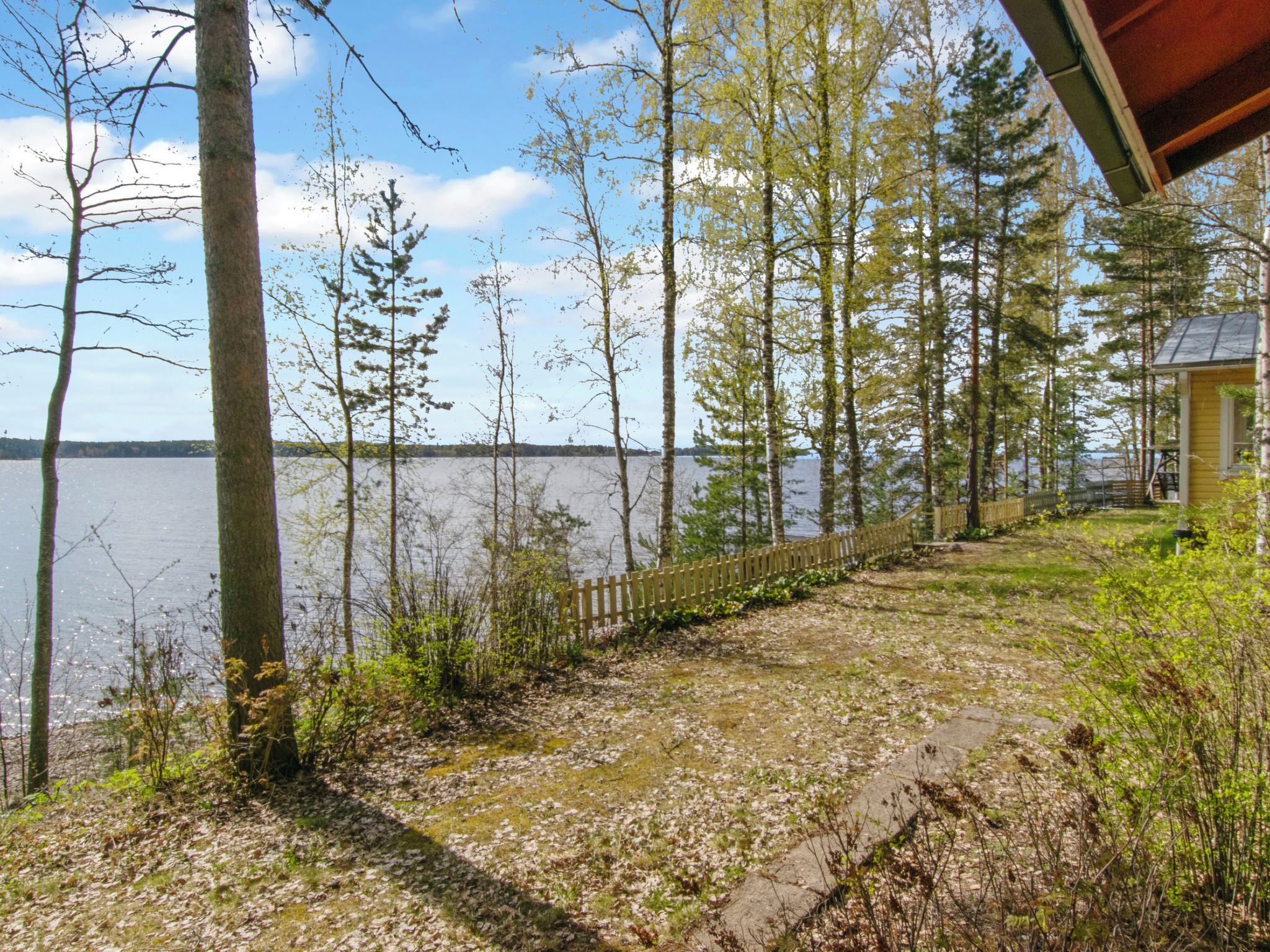 A lakeside property with a wooden deck, a wooden fence, and a small cabin.