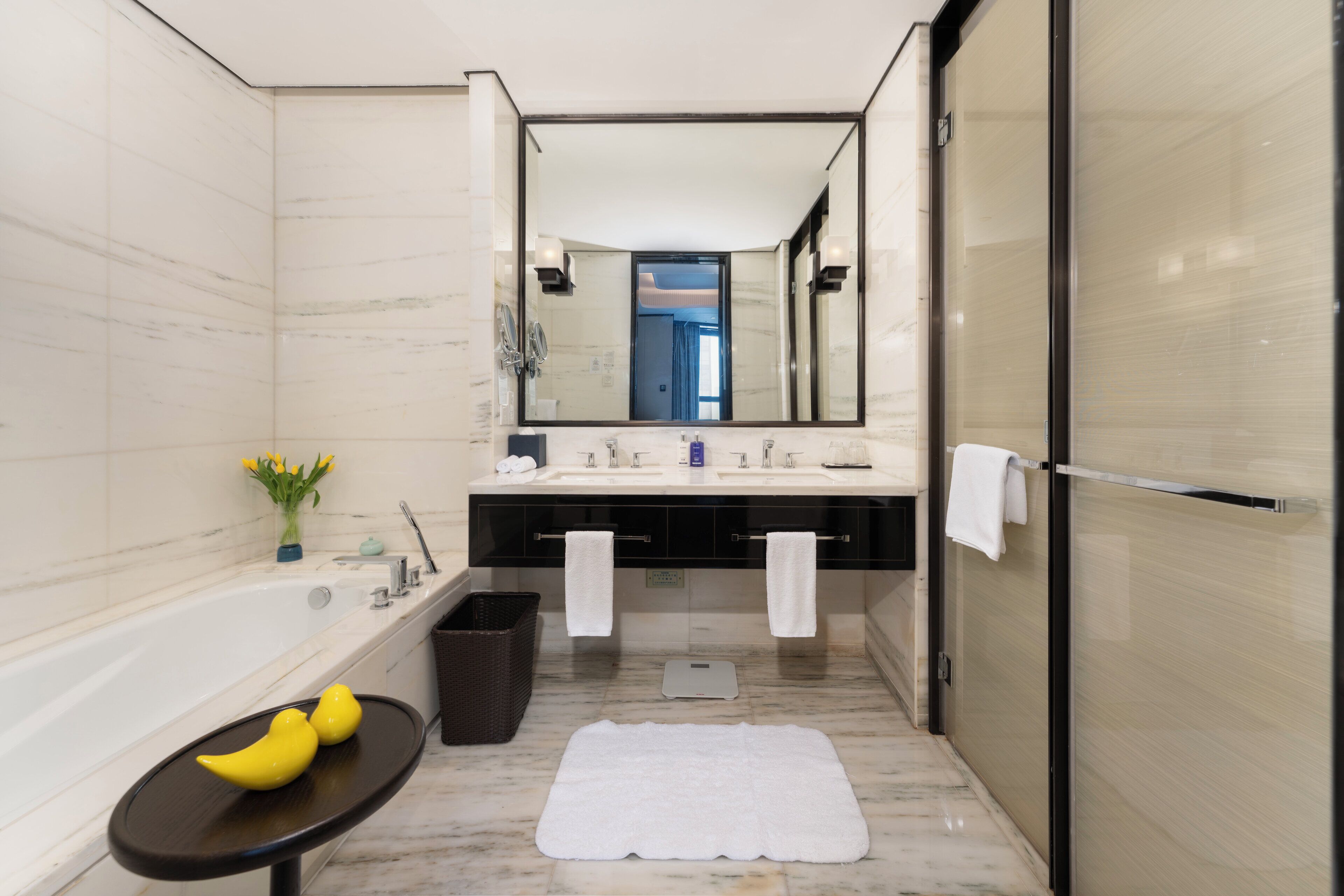 A modern bathroom with a bathtub, dual sinks, a large mirror, and a vanity with a towel rack.