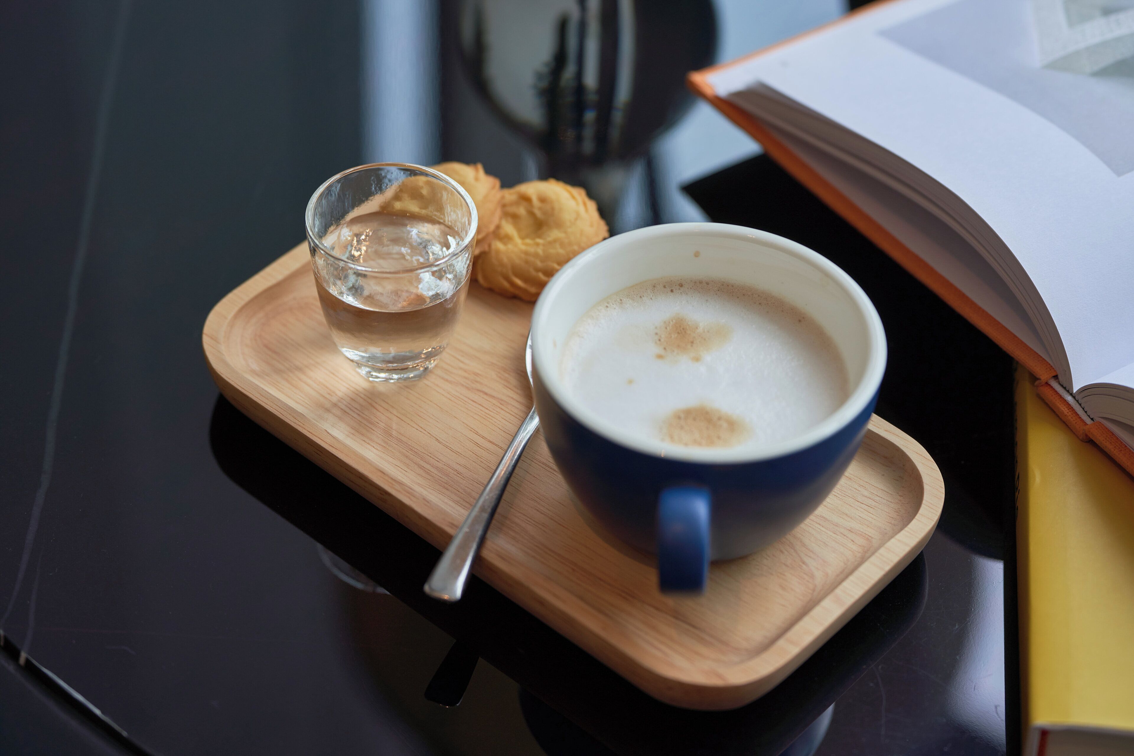 A cup of coffee on a wooden tray with a biscuit and a glass of water.