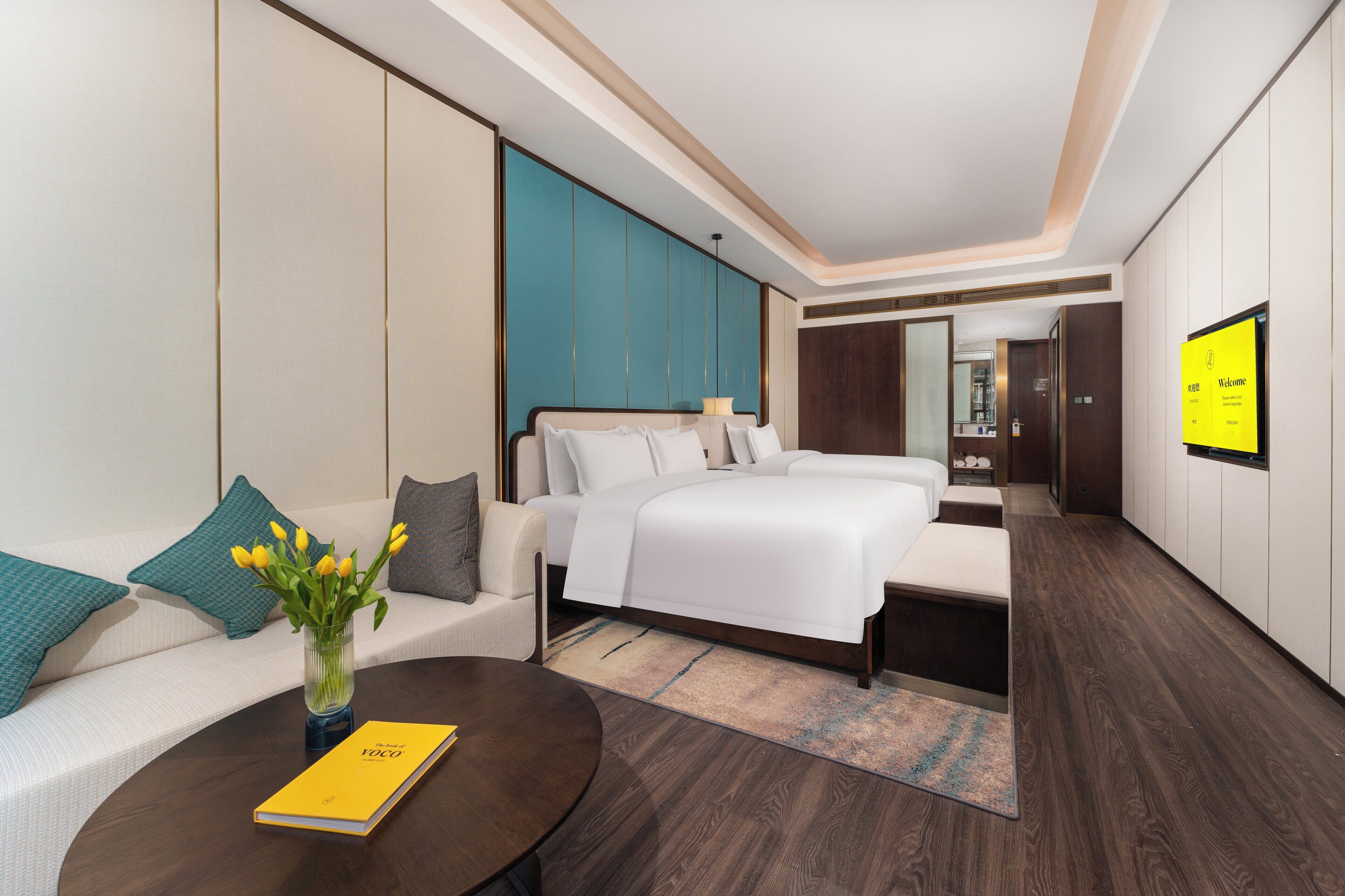 Quarto de hotel moderno com cama, sofá e uma mesa de centro com um livro.