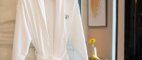 A white bathrobe hanging on a wooden hanger in a room with a marble wall and a framed artwork.