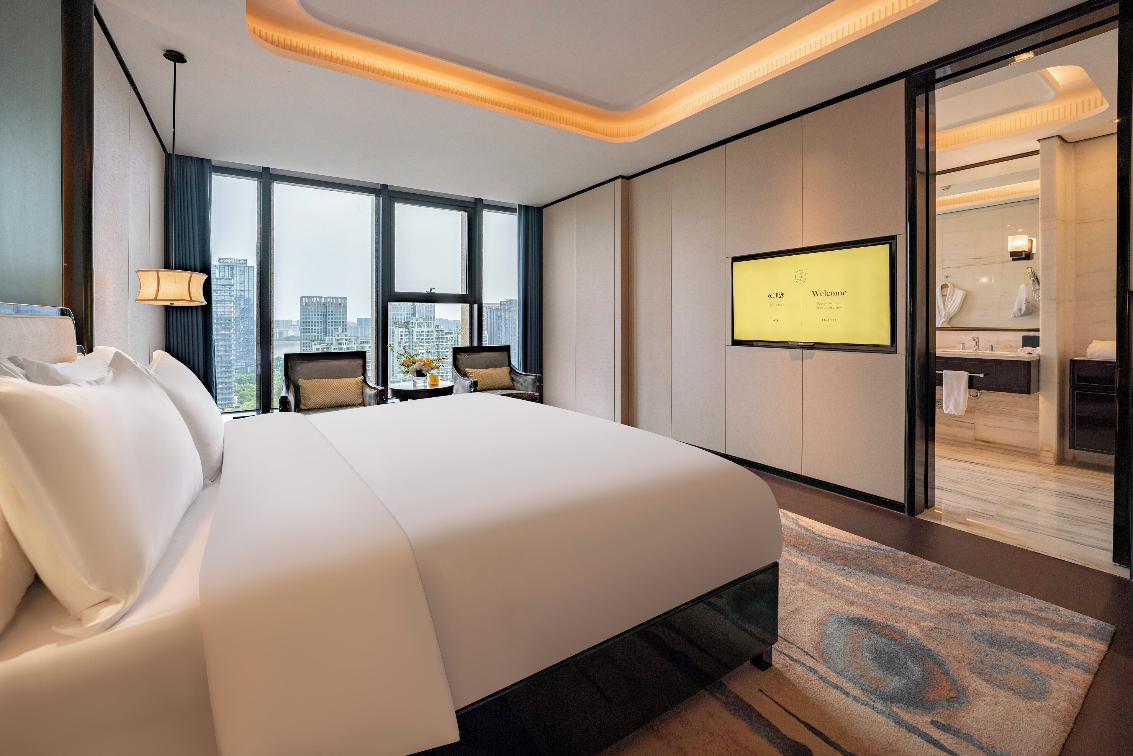 Una habitación de hotel moderna con una cama grande, un escritorio con silla, televisión y vistas a la ciudad.