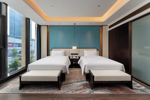 A modern hotel room with a large bed, two bedside tables, a nightstand, and a view of the city.