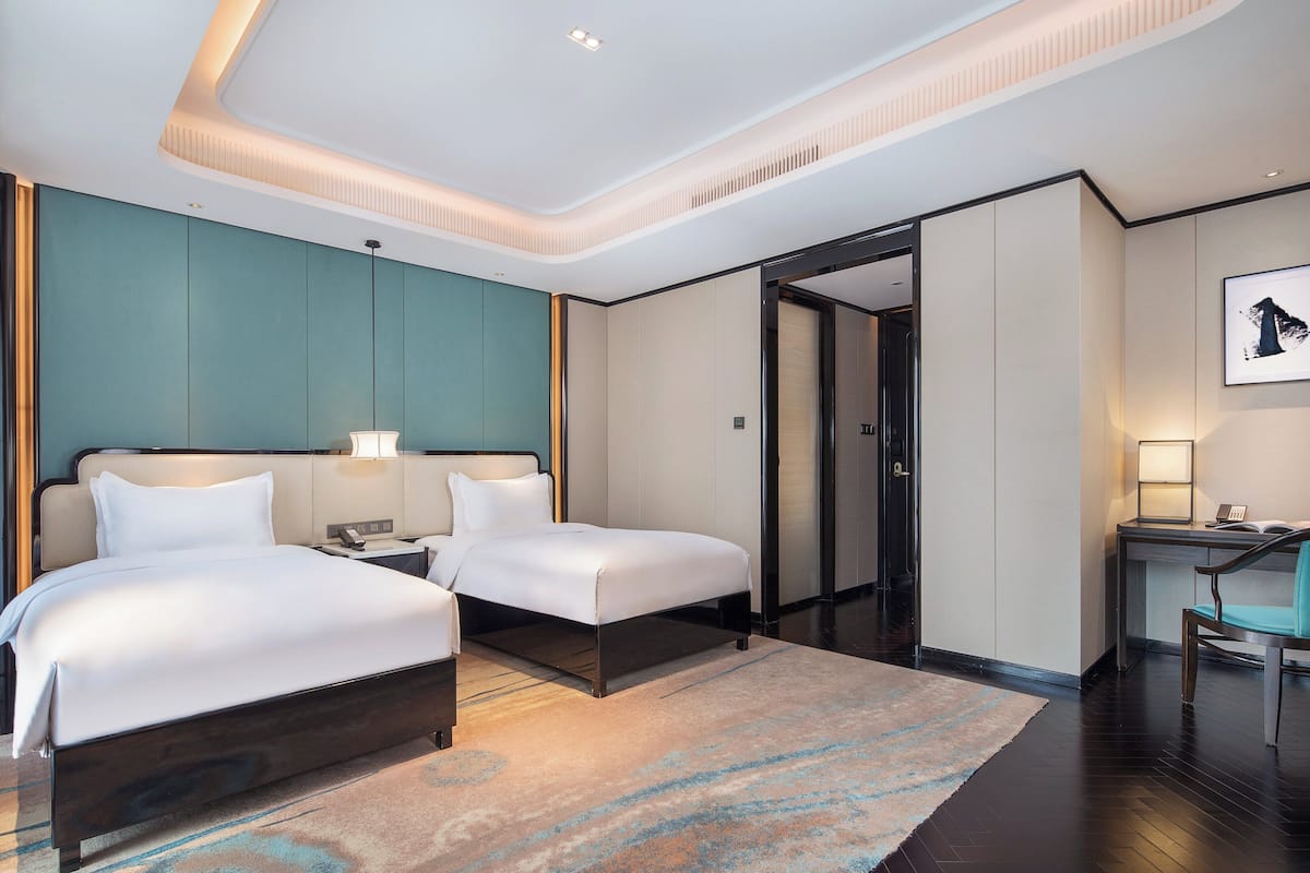 Une chambre d’hôtel moderne équipée de deux lits, d’un bureau, d’une chaise et d’une porte de salle de bain.