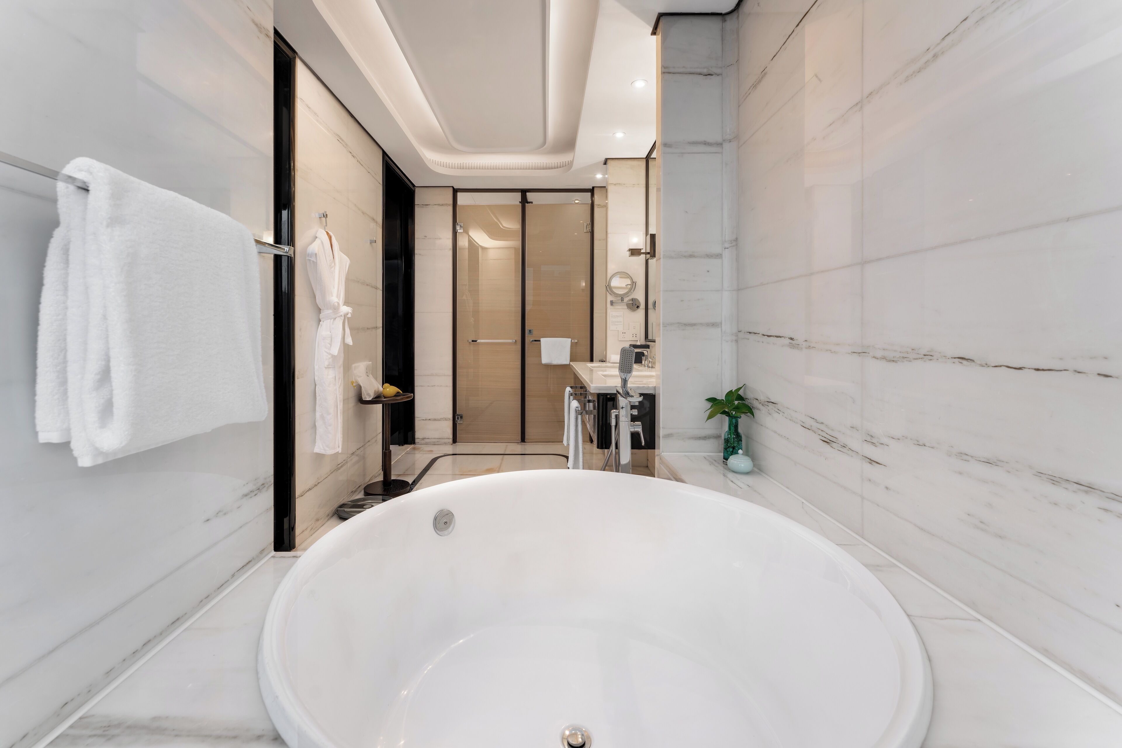 A modern bathroom with a large bathtub, a glass shower enclosure, and a marble-tiled wall.