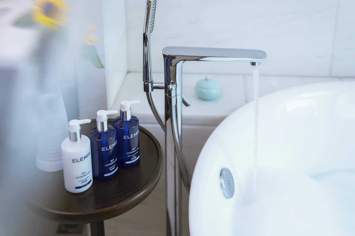 Une salle de bain avec une baignoire blanche, un miroir rond et des articles de toilette disposés sur une petite table.