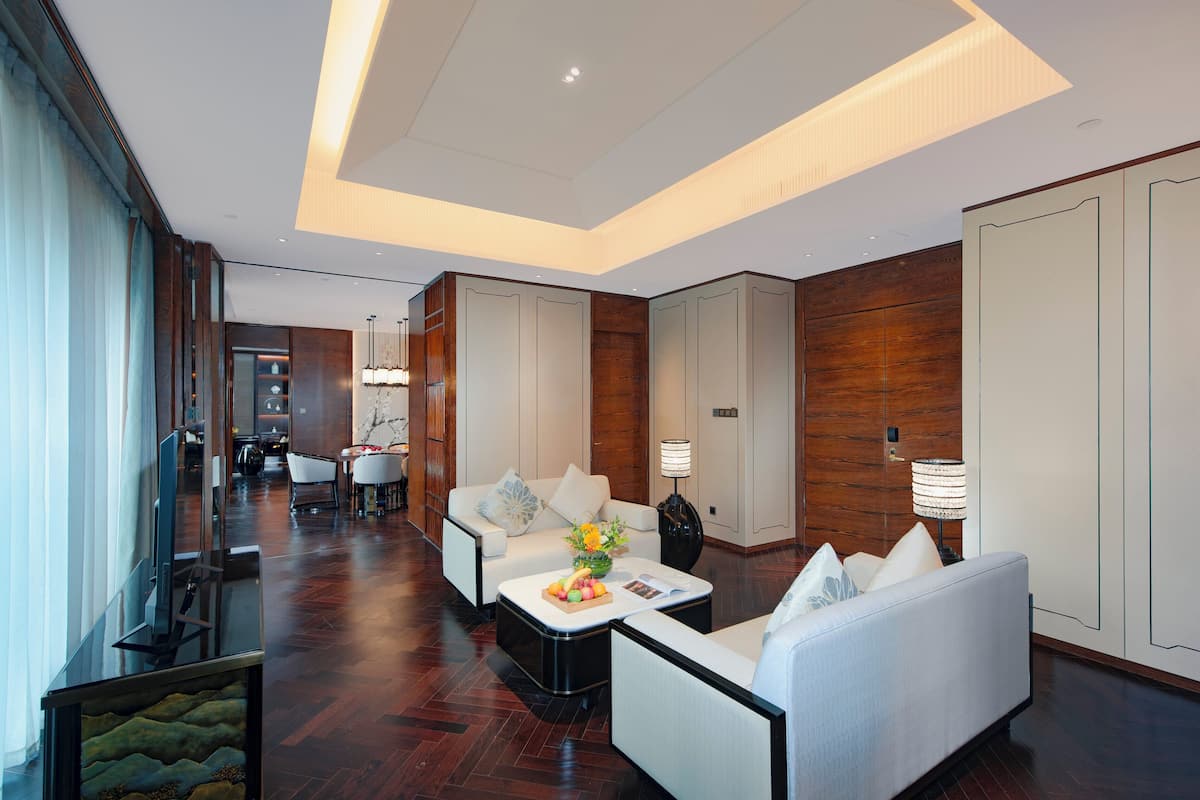Un hall d’hôtel spacieux au design moderne, comprenant un coin salon avec des canapés et une table basse, un comptoir de réception et une vue sur le couloir.