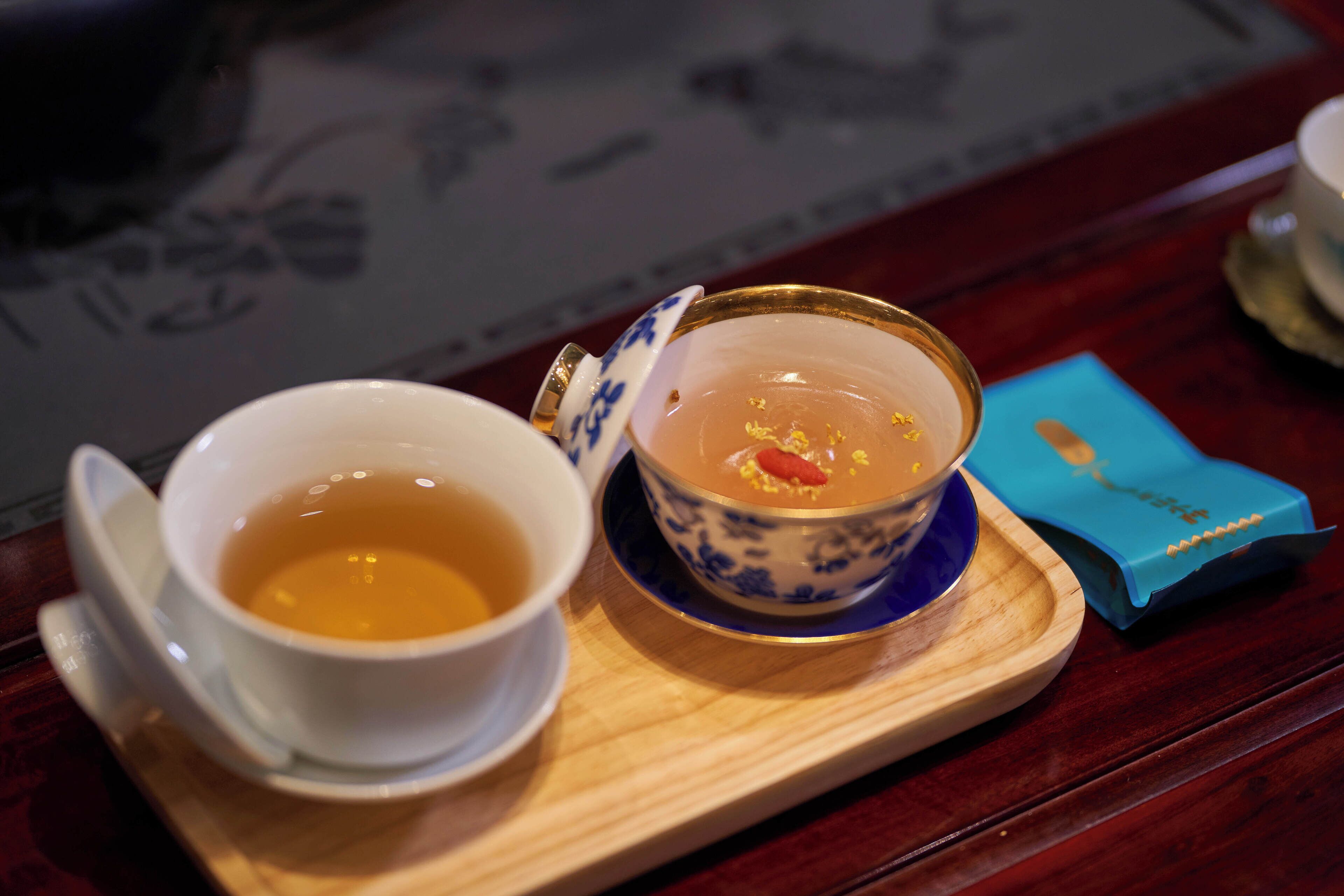 Deux tasses de thé sur un plateau en bois, l’une avec un motif bleu et l’autre de couleur blanche unie.