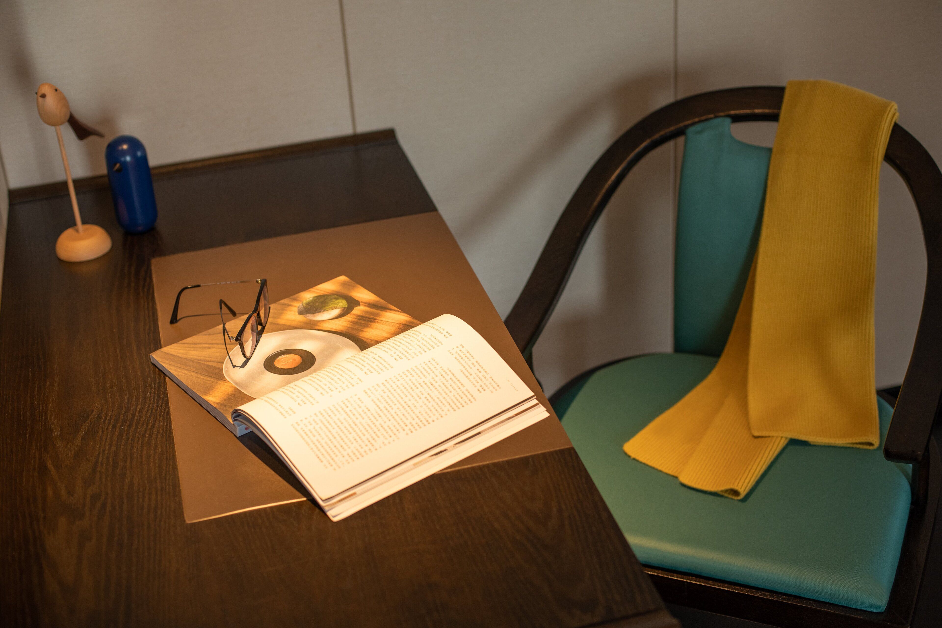 A wooden table with a book, glasses, and a blue object.