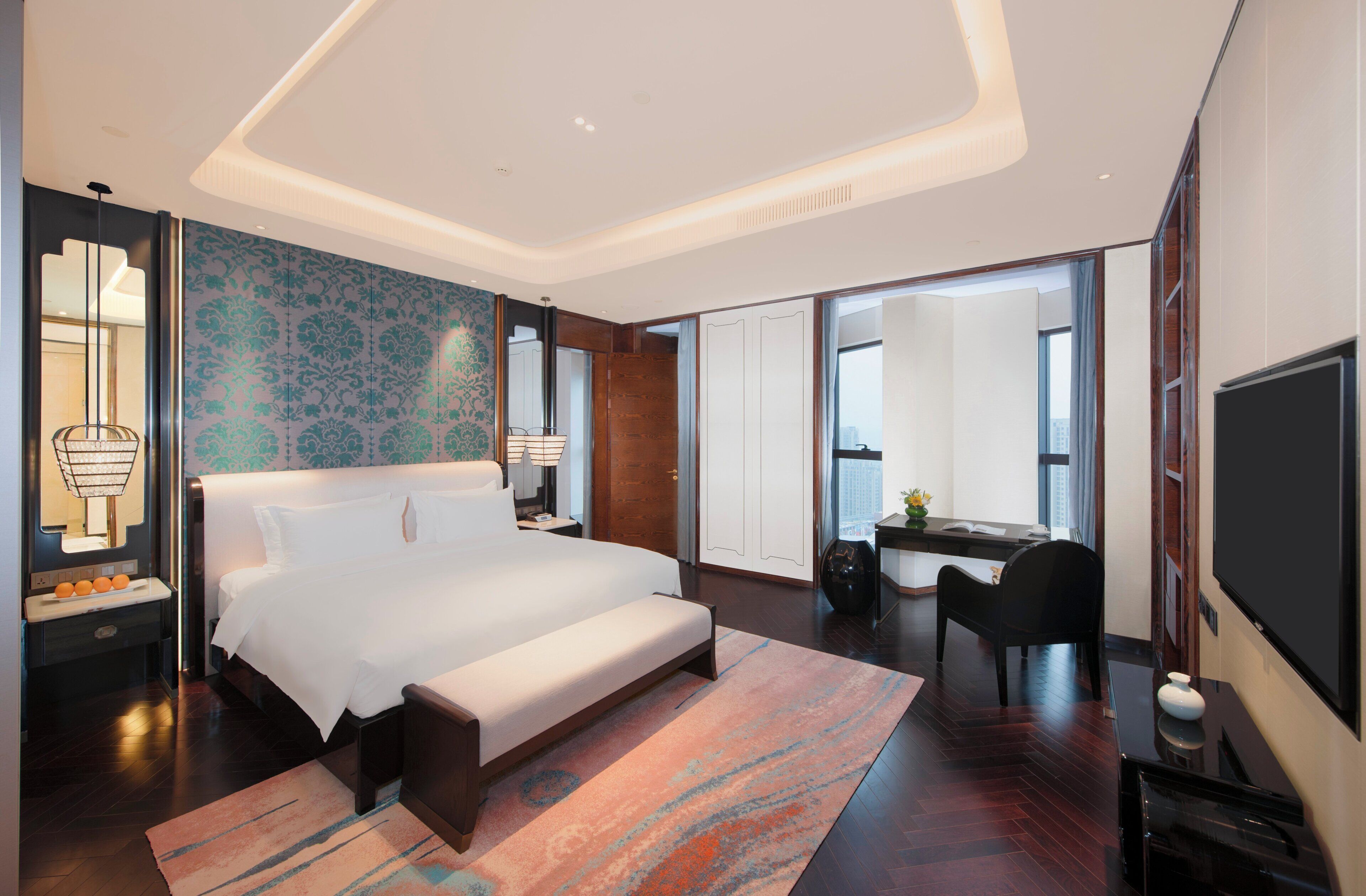 A modern hotel room with a large bed, a desk, a chair, and a television.