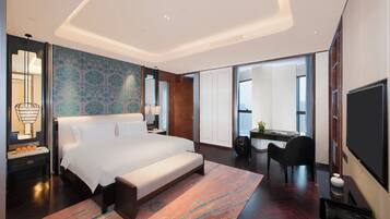 A modern hotel room with a large bed, a desk, a chair, and a television.