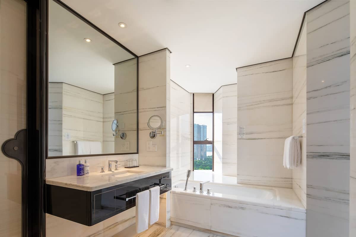 Une salle de bain moderne dotée d’un grand miroir, d’une baignoire et d’une fenêtre donnant sur la ville.