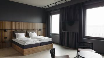 Una habitación de hotel moderna con cabecera de madera, una cama grande, televisor de pantalla plana, una mesa redonda y una silla.