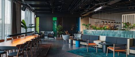 Un espacio de oficina moderno con una larga mesa de madera y sillas, un área de descanso con sofás y una mesa baja, y una pared decorativa con plantas.