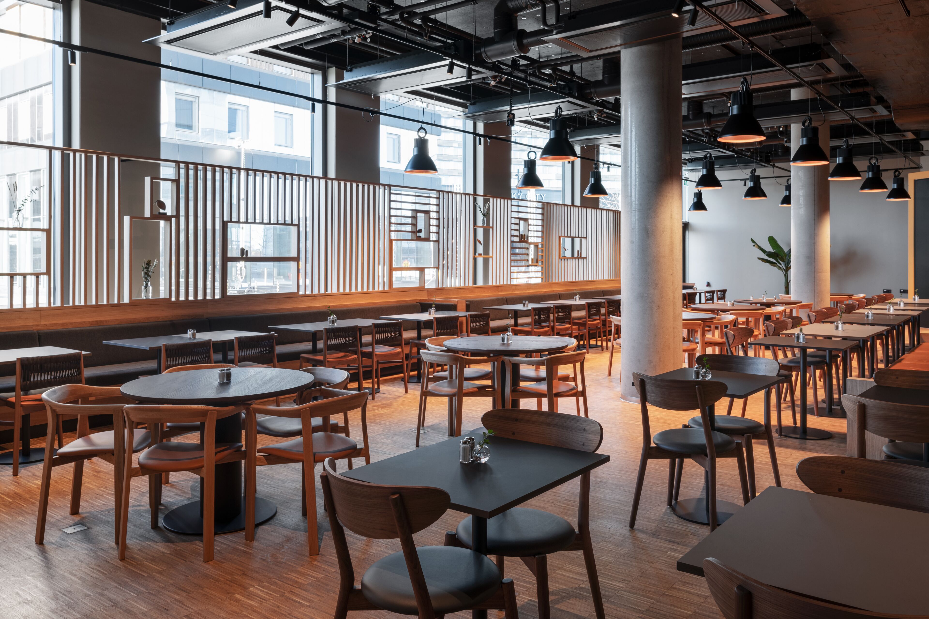 Een ruim restaurant met hoge plafonds, grote ramen en diverse zitmogelijkheden, waaronder tafels en zitbanken.