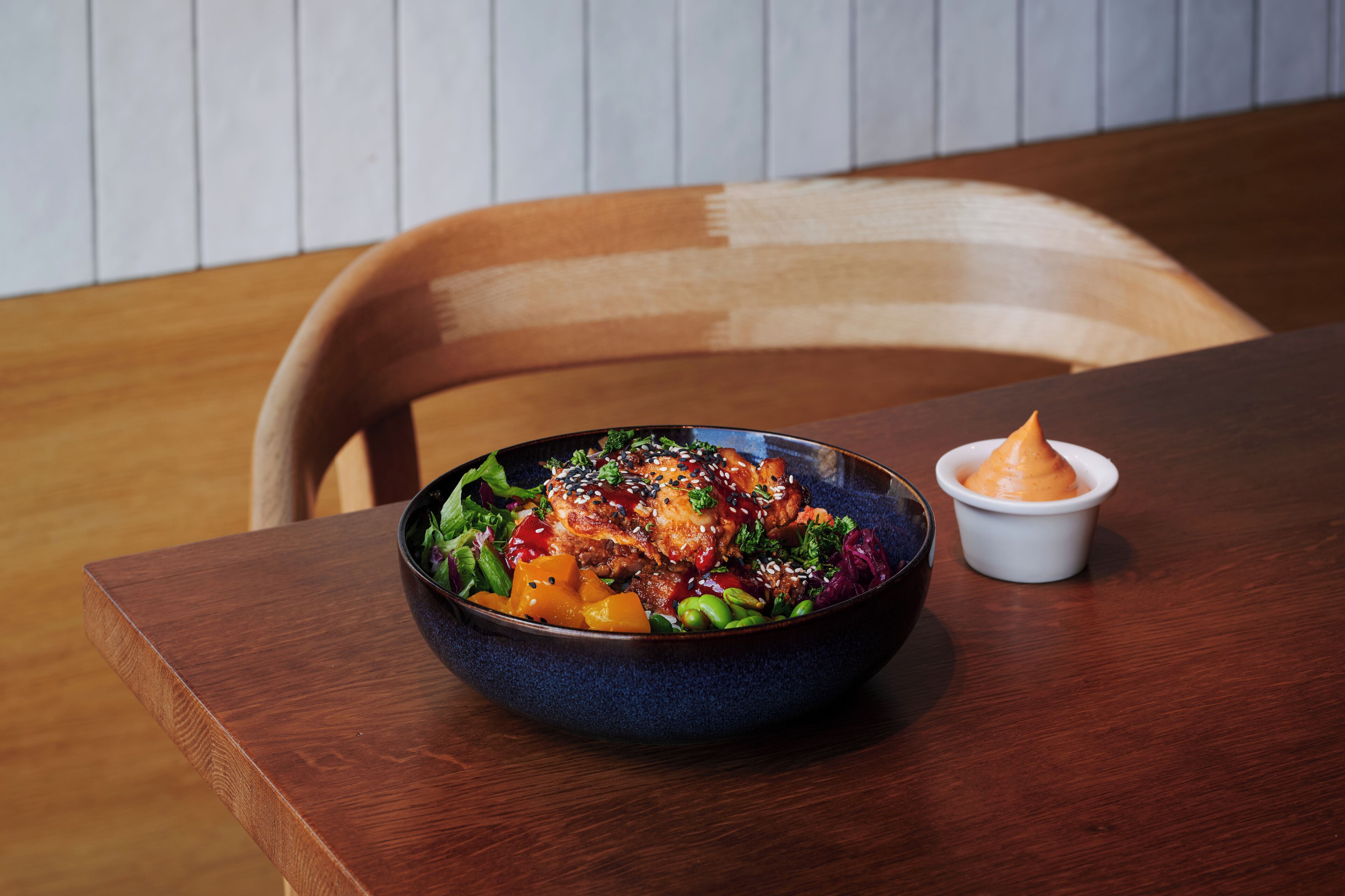 A bowl of food on a wooden table with a chair in the background.