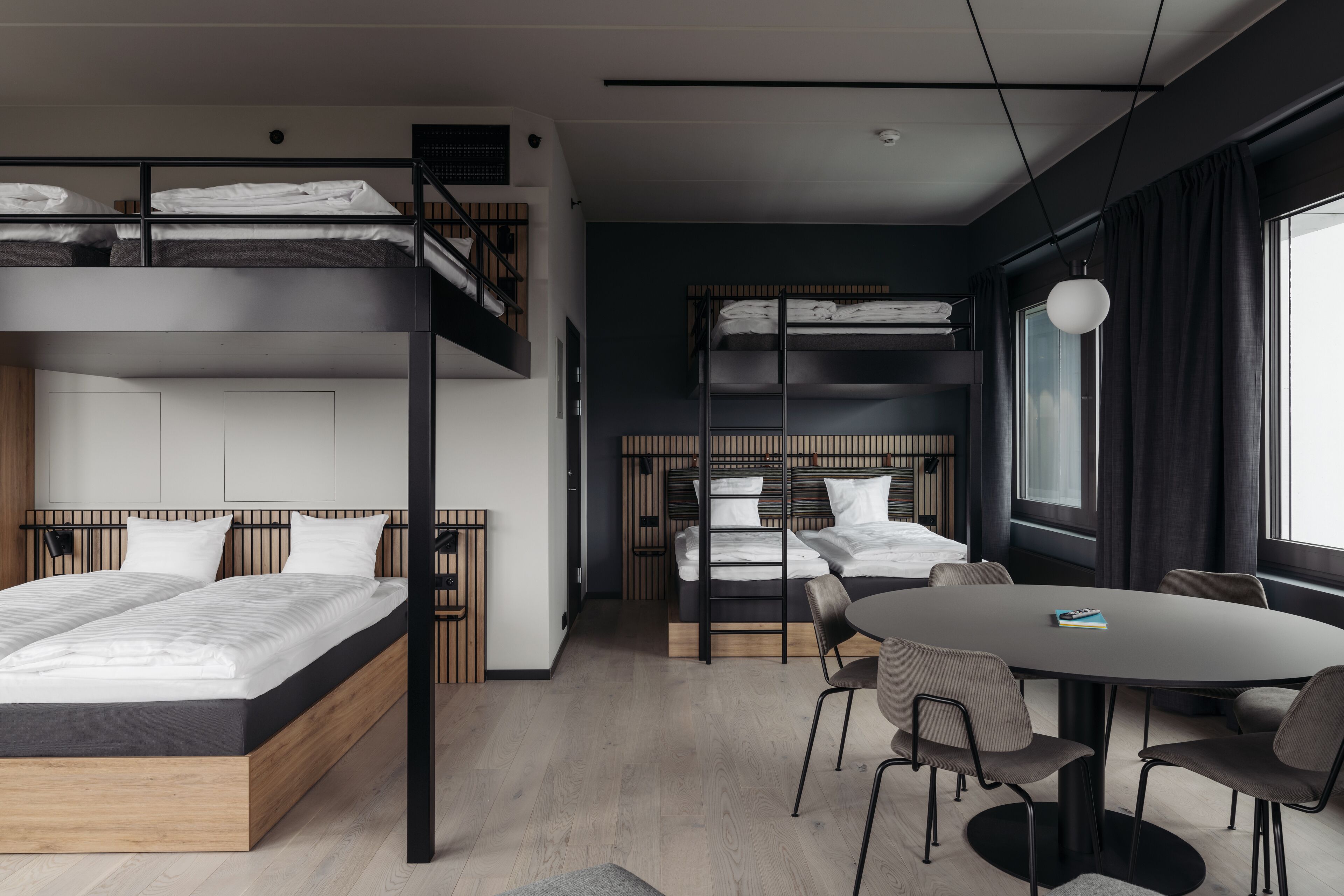 Een moderne hotelkamer met stapelbedden, een eettafel en een groot raam.