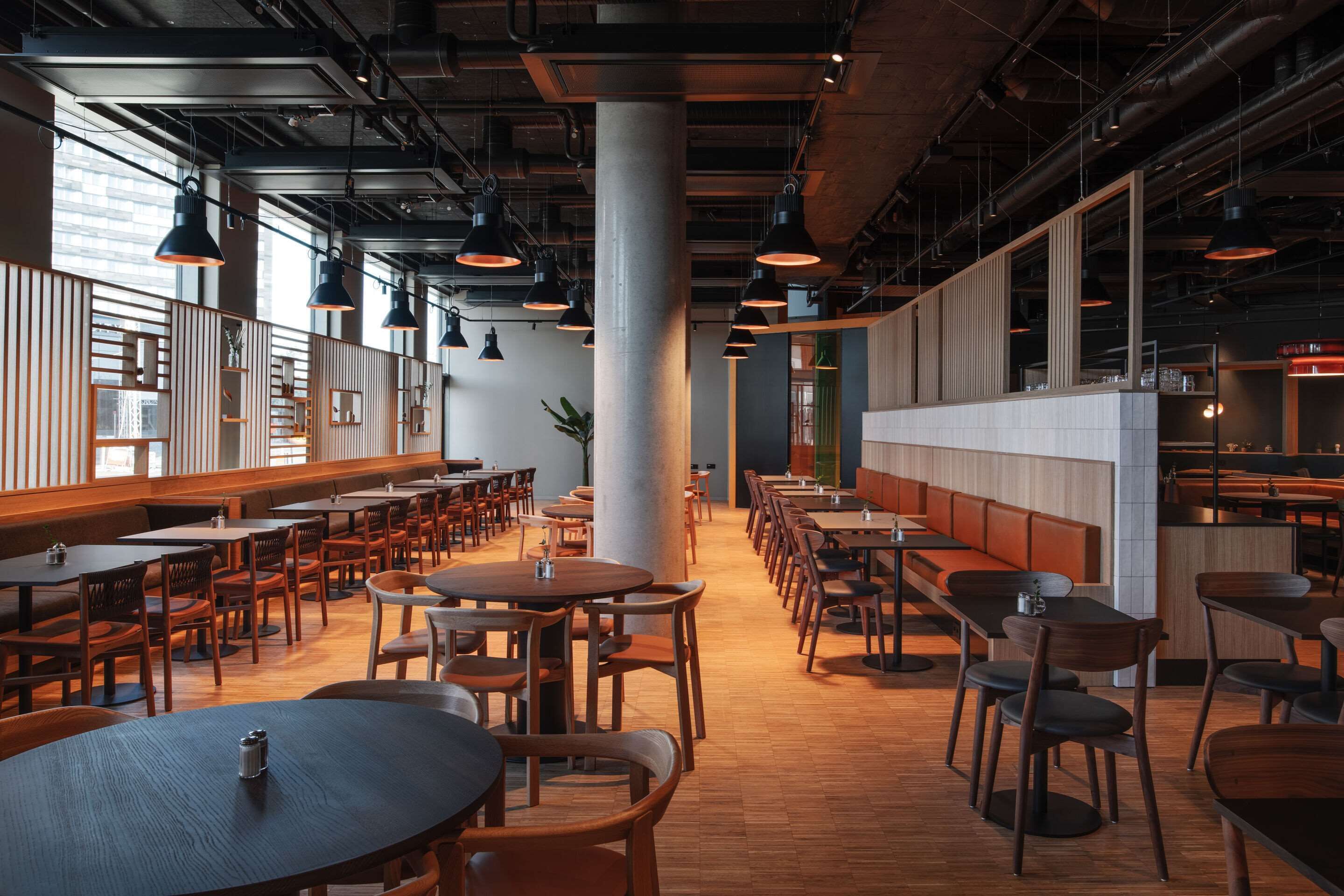 En rymlig restaurang med högt i tak, synliga ventilationskanaler och en blandning av möbler i trä och metall.