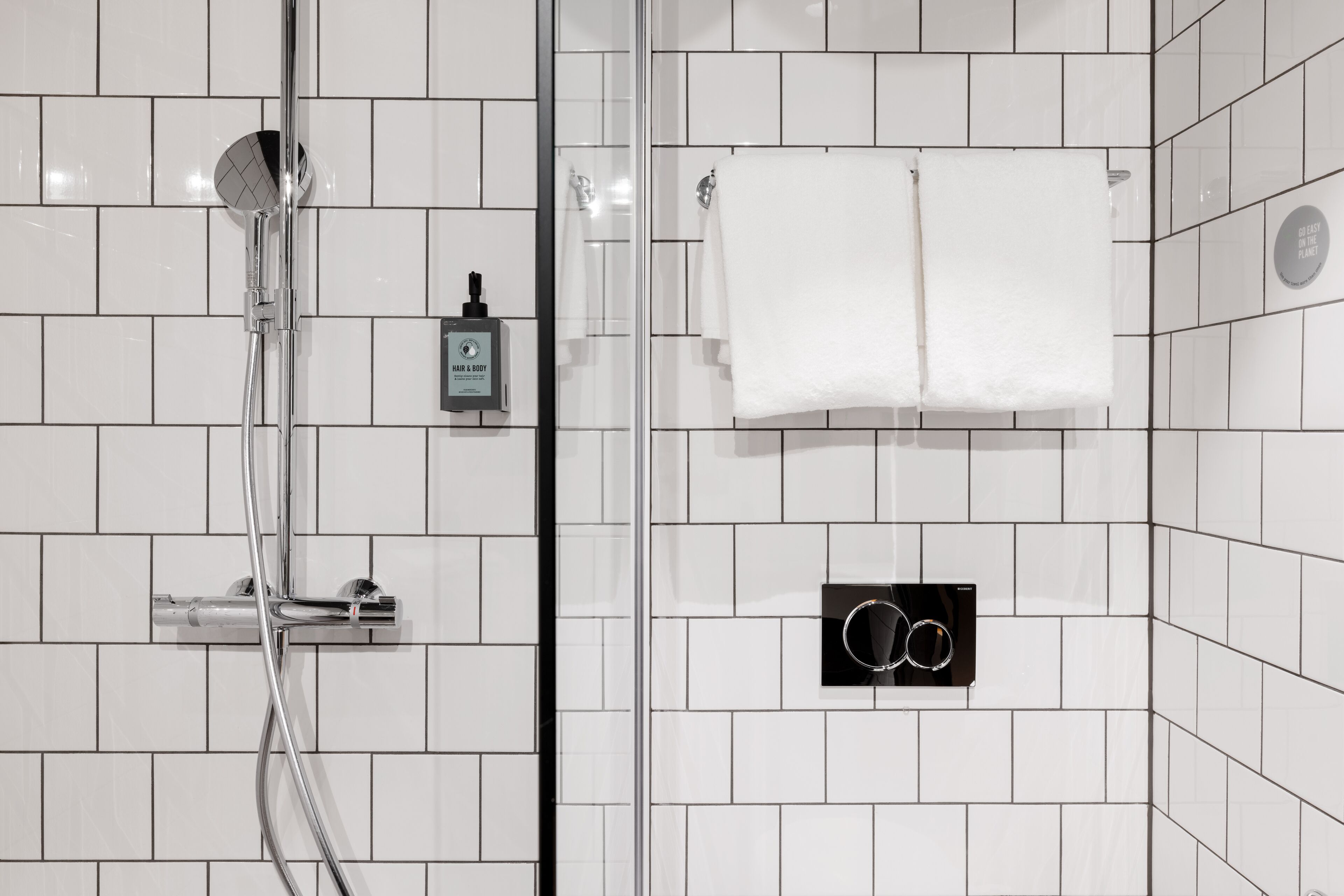 Un baño moderno con azulejos blancos, ducha con mampara de vidrio, toallero y dispensador de jabón.
