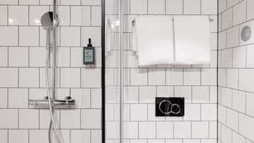 Un baño moderno con azulejos blancos, ducha con mampara de vidrio, toallero y dispensador de jabón.